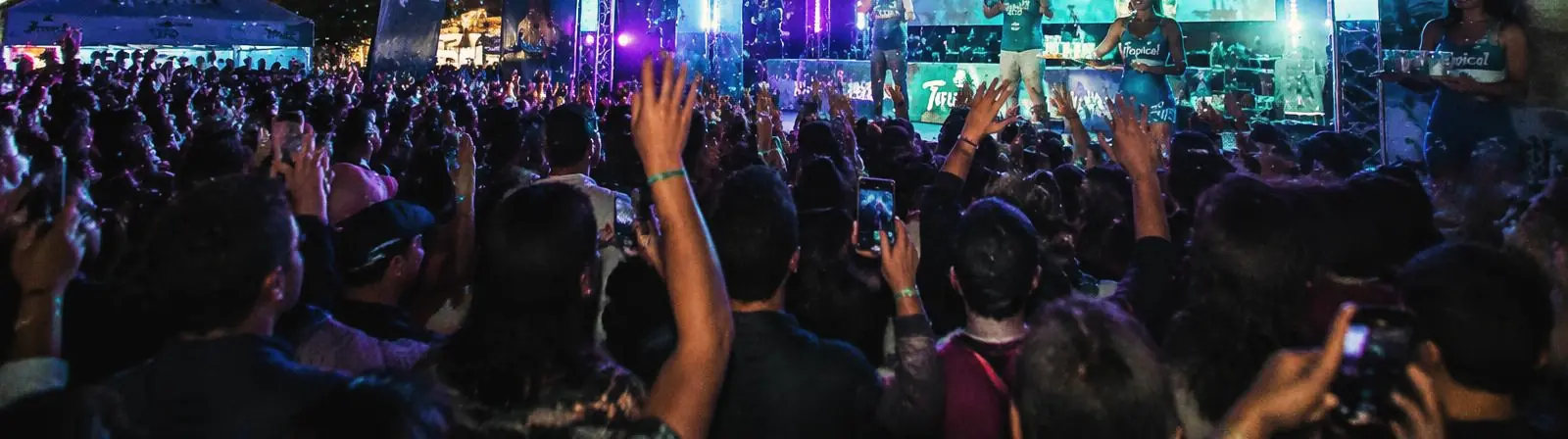 Público con las manos en alto frente a un escenario iluminado durante una activación nocturna