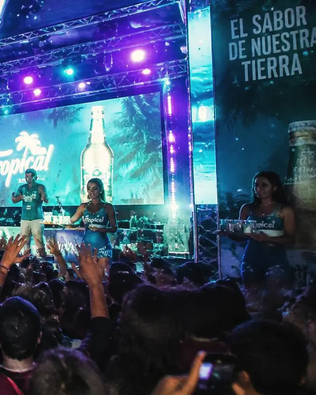 Promotoras con bandejas frente a un escenario iluminado durante una activación nocturna